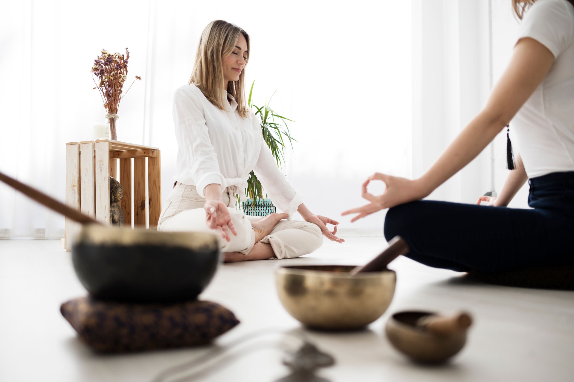 A yoga teacher and her student meditate sitting across from each other.