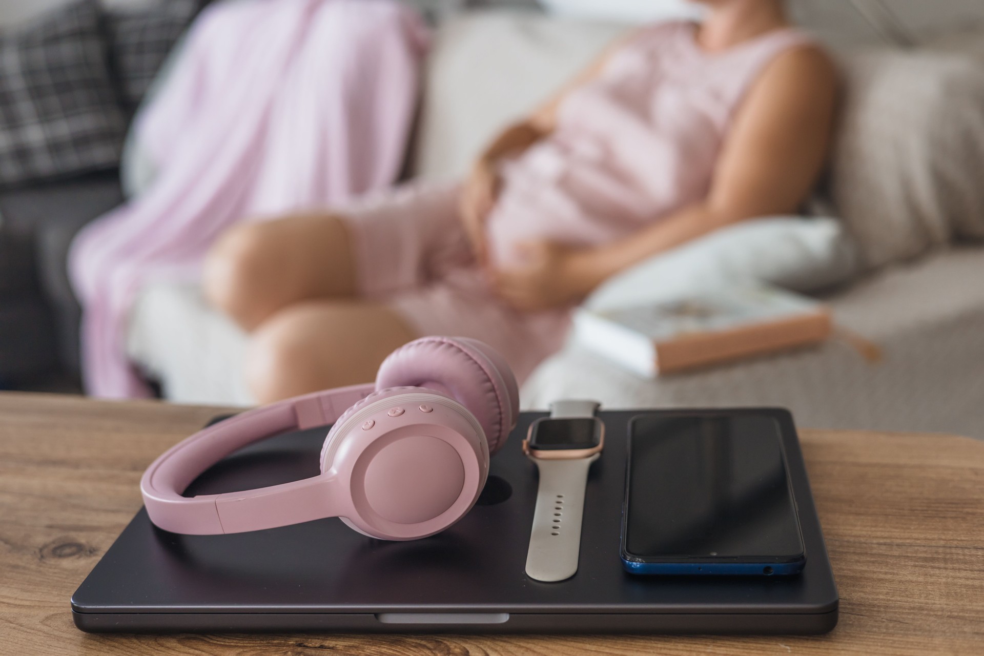 Digital detox during a cozy afternoon at home with headphones and a book in hand. Pregnant woman relaxing on coach