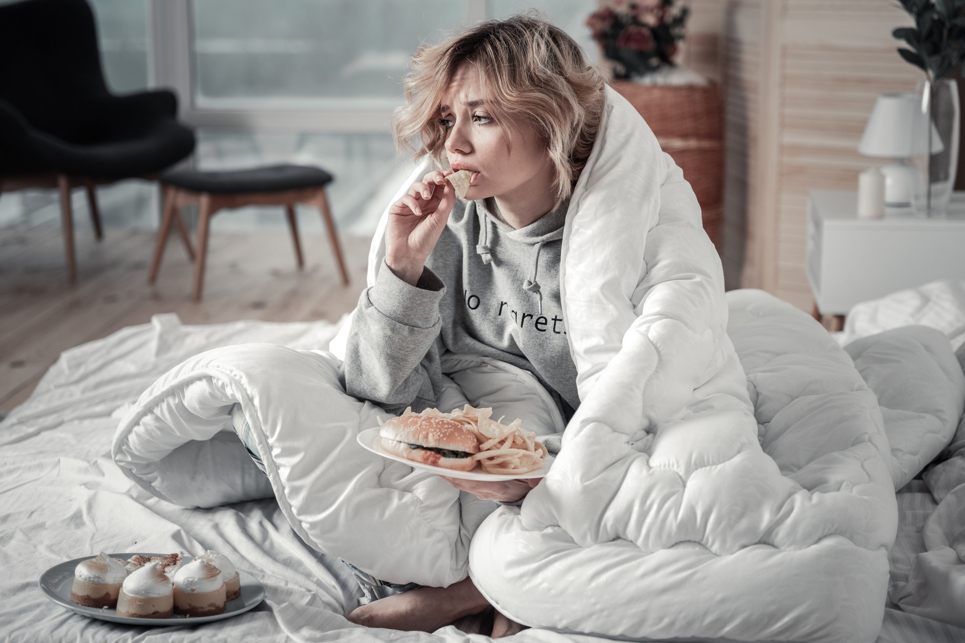 Sad and lonely woman eating burger and French fries in the bed